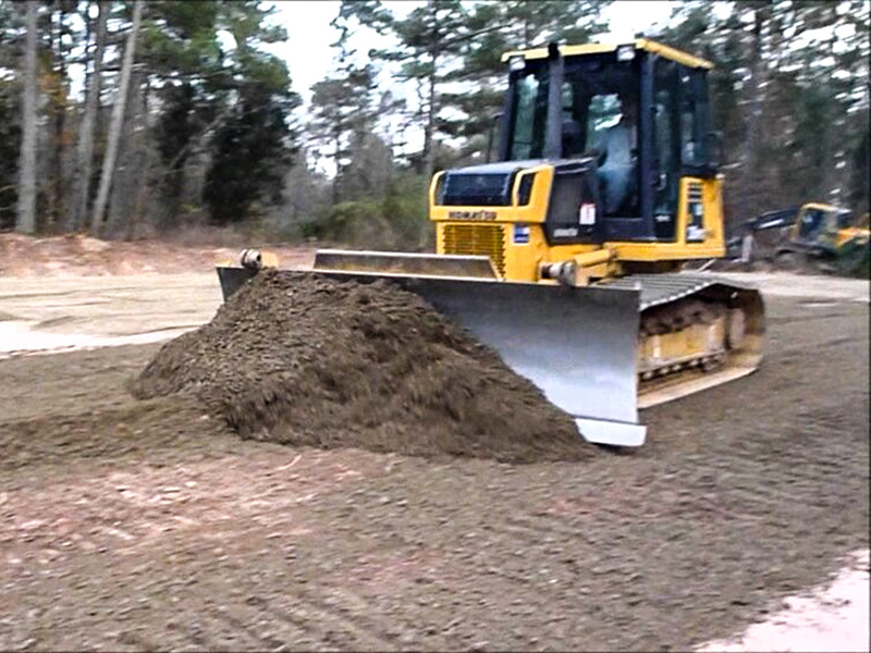 Bulldozer-Grading A yellow Komatsu bulldozer with a large front blade is pushing a pile of dark brown dirt on a construction site.